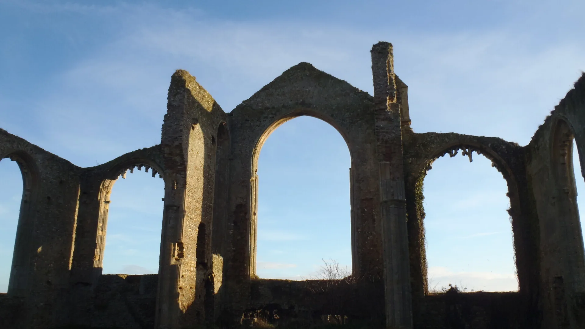 The ruin of St. Andrew's Covehithe photographed as a silhouette of several adjoining arches against a bright blue sky.