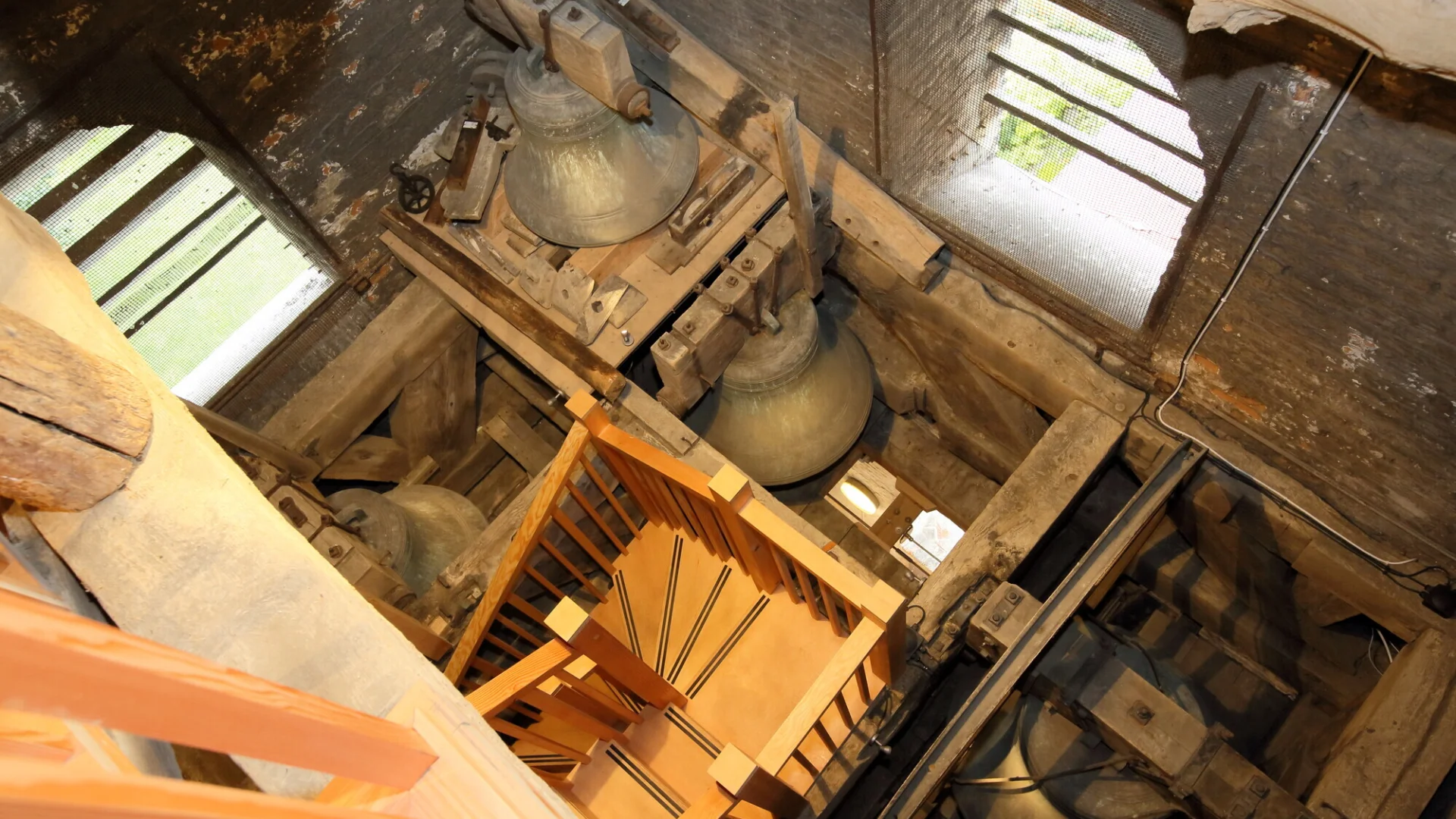 Interior view of the bell tower at St. Peter's, Sandwich in Kent. The photograph is taken from an elevated position looking down at the bells. A wooden staircase leads down to the bells.