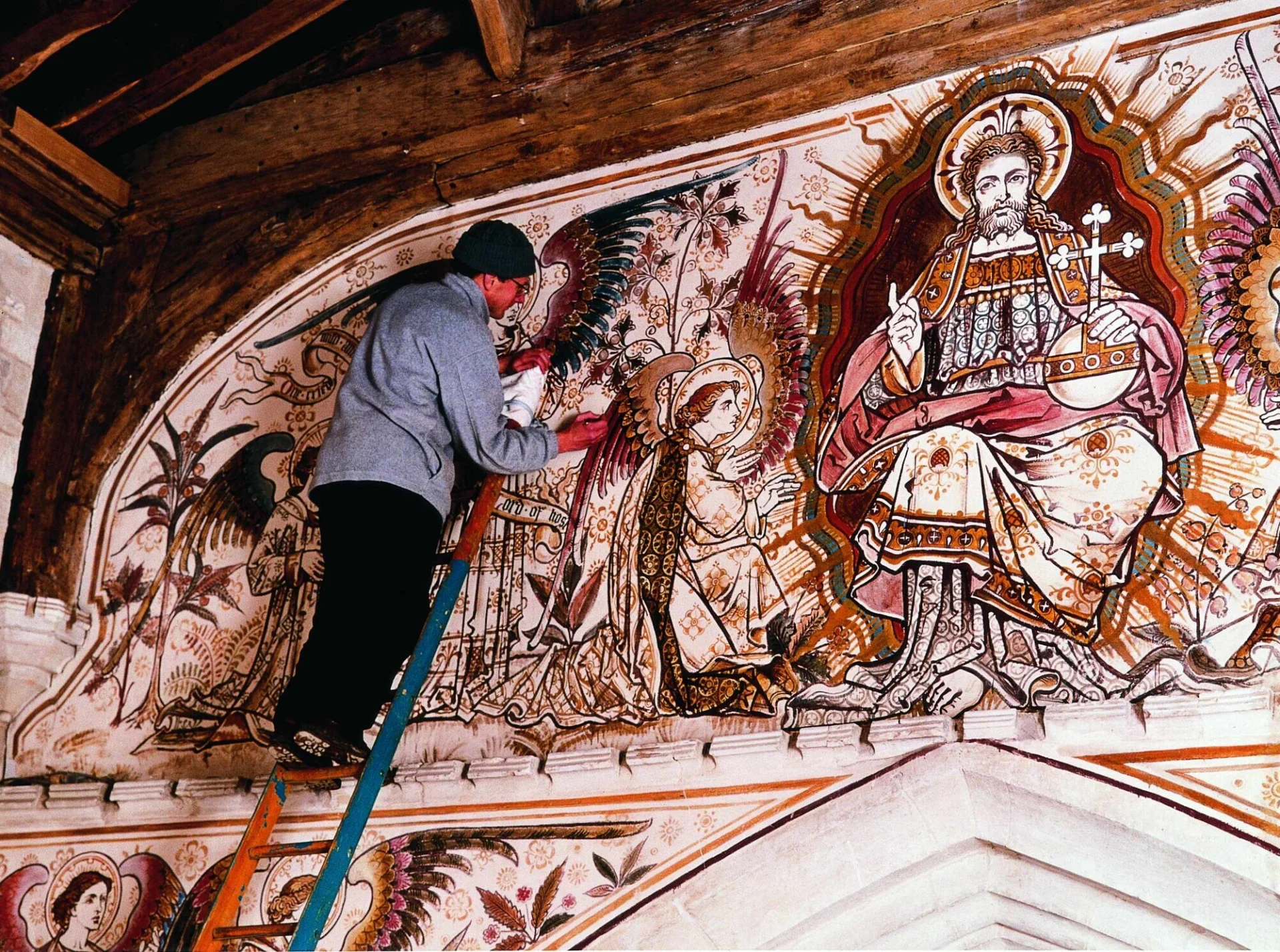 Conservator up a ladder delicately working on a large wall painting at Edlesborough, depicting an angel worshiping.