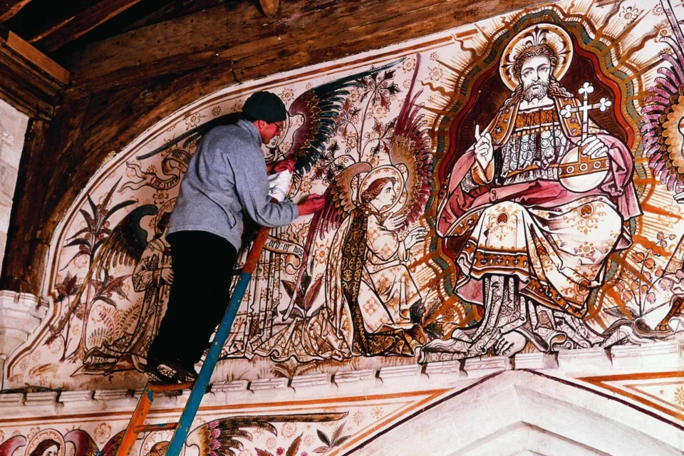 Conservator up a ladder delicately working on a large wall painting at Edlesborough, depicting an angel worshiping.