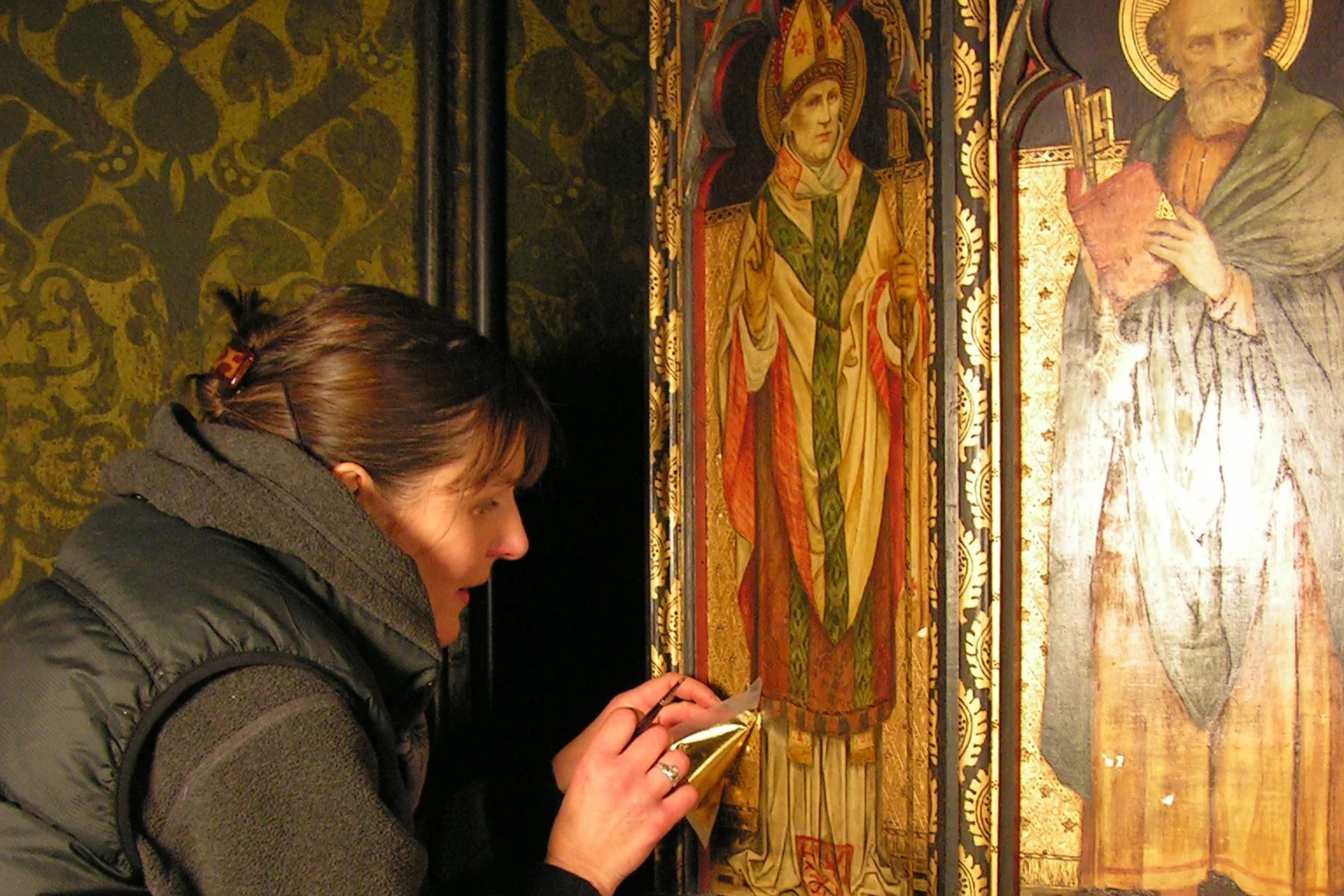 Conservator working on a wall painting of a saints at All Saints Church in Cambridge.