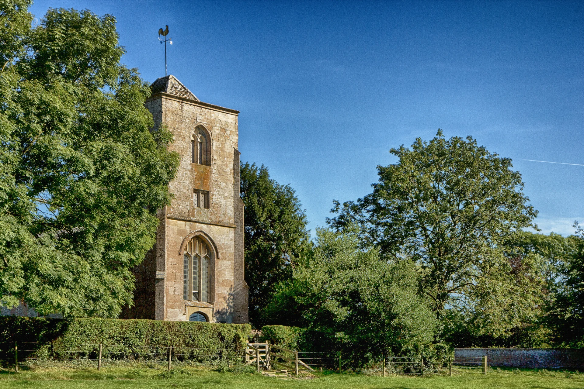 A stunning church towers above a beautiful field and lush trees