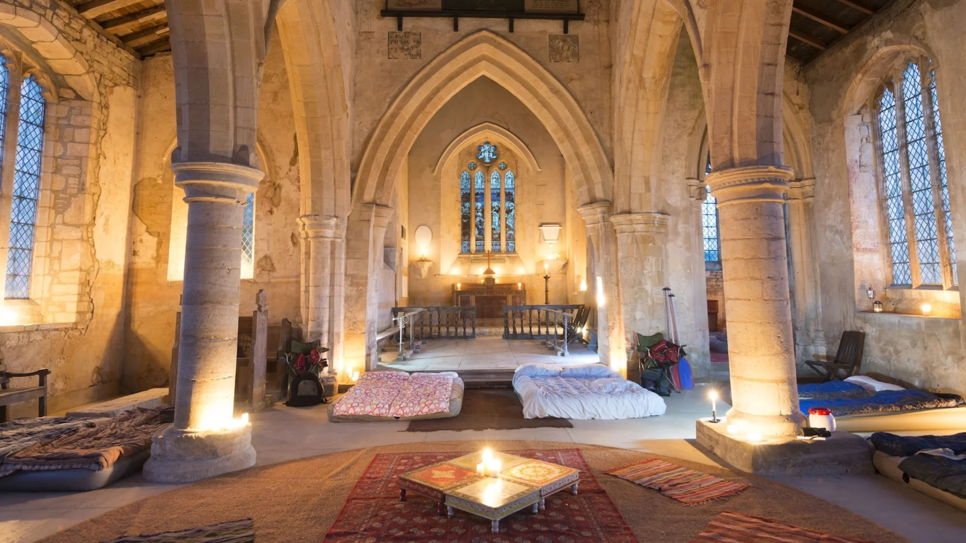 candle lit church interior with beautiful stone arches and large windows. Mattresses on floor.