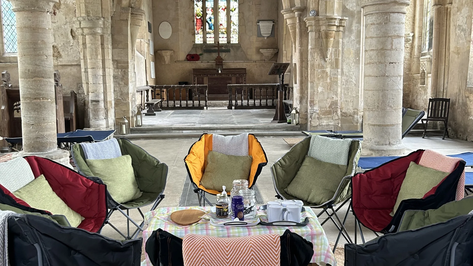 Interior of church with camping chairs arranged in a circle around a coffee table, set up for tea.
