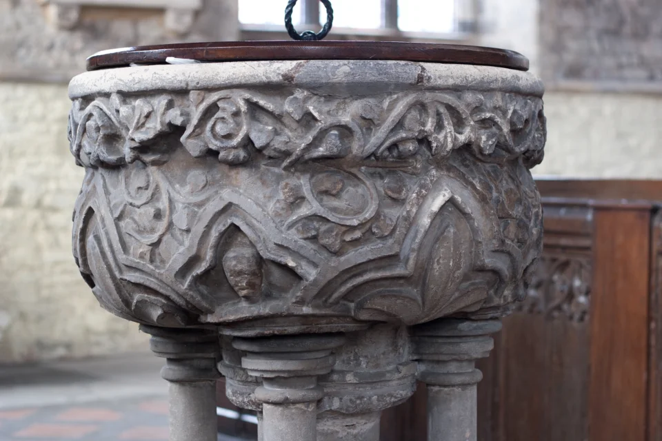 richly carved thirteenth-century stone font with leaves, vines, and faces