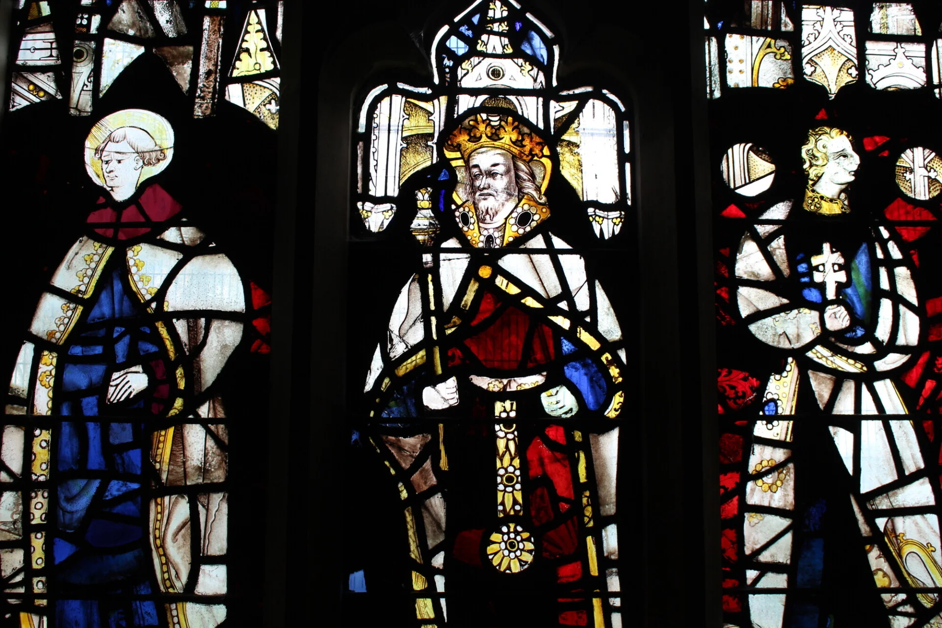 Stained glass window showing a monk, a king and a third figure carrying a cross. Dominant colours are red, blue, yellow.