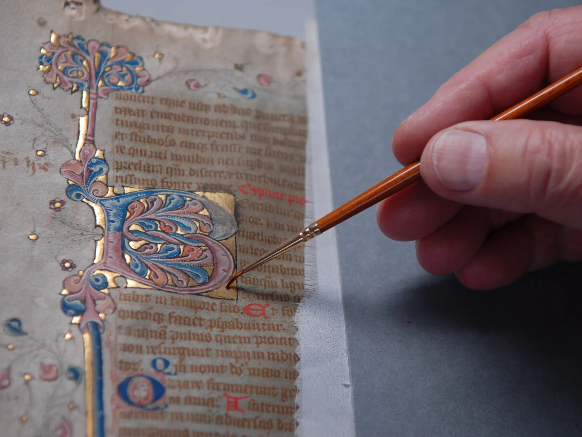 A hand holds a delicate paintbrush works on the gold lettering on a bible