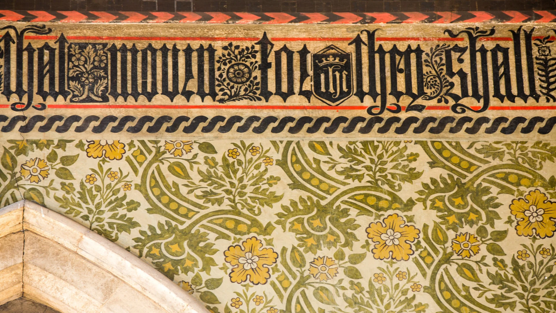 Victorian Wall paintings in a church showing green and yellow scrolling flowers and foliage, and gothic text in orange, black and white colours.