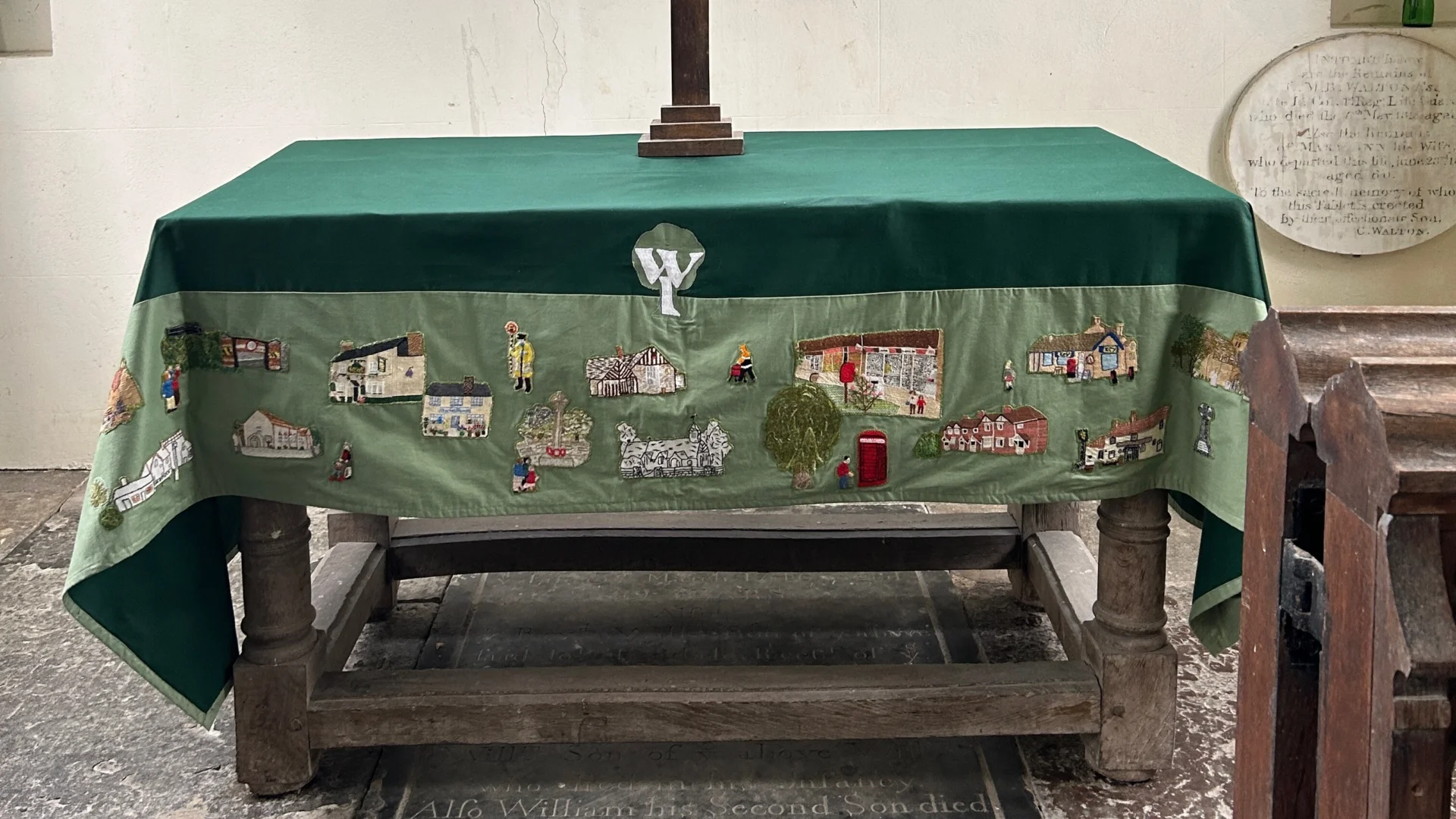 Altar with green altar cloth covered in sown on patches to represent local buildings made by the local WI