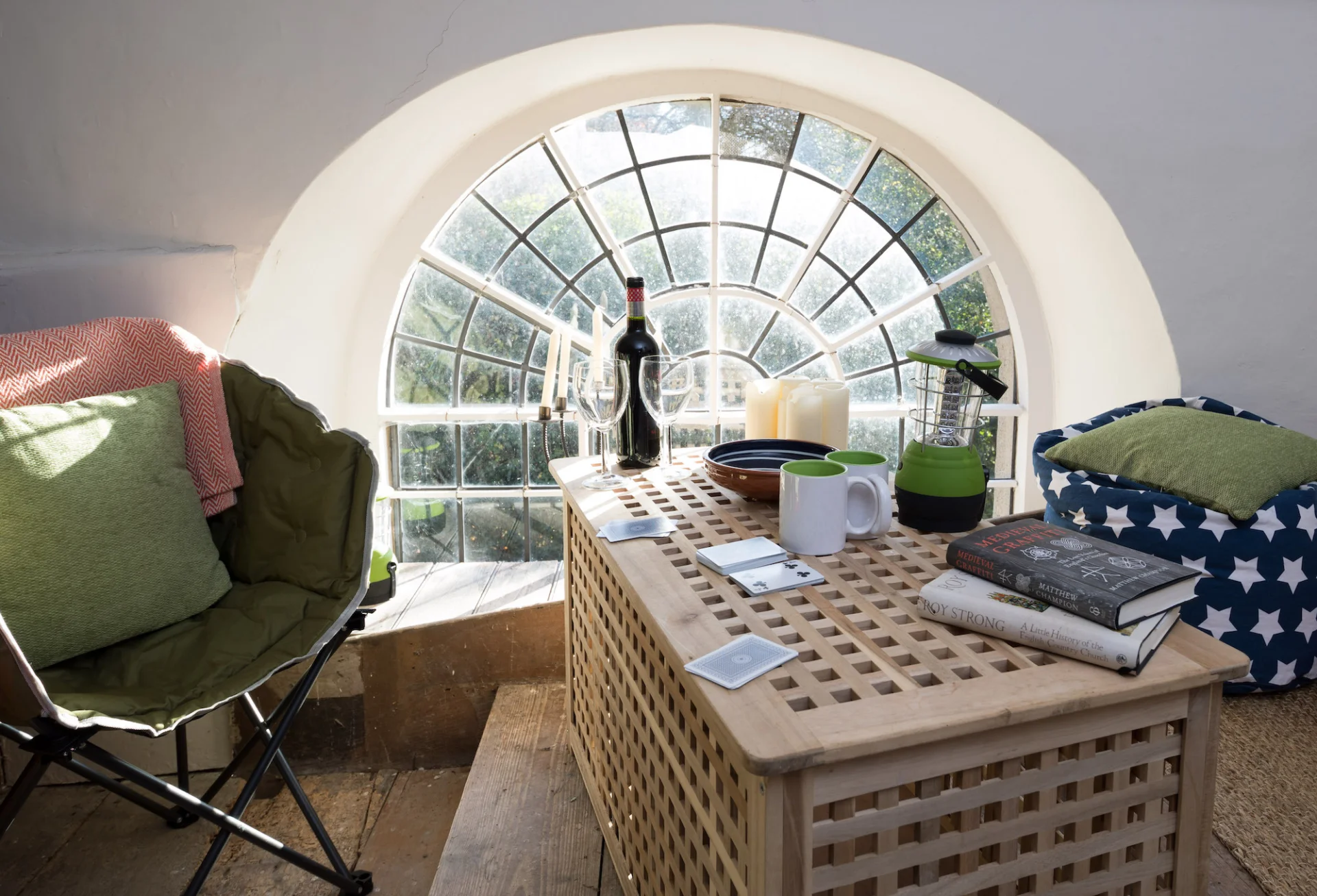 Champing set up with a chair and bean bag sitting area with little pillows table with wine glass and a large wine.