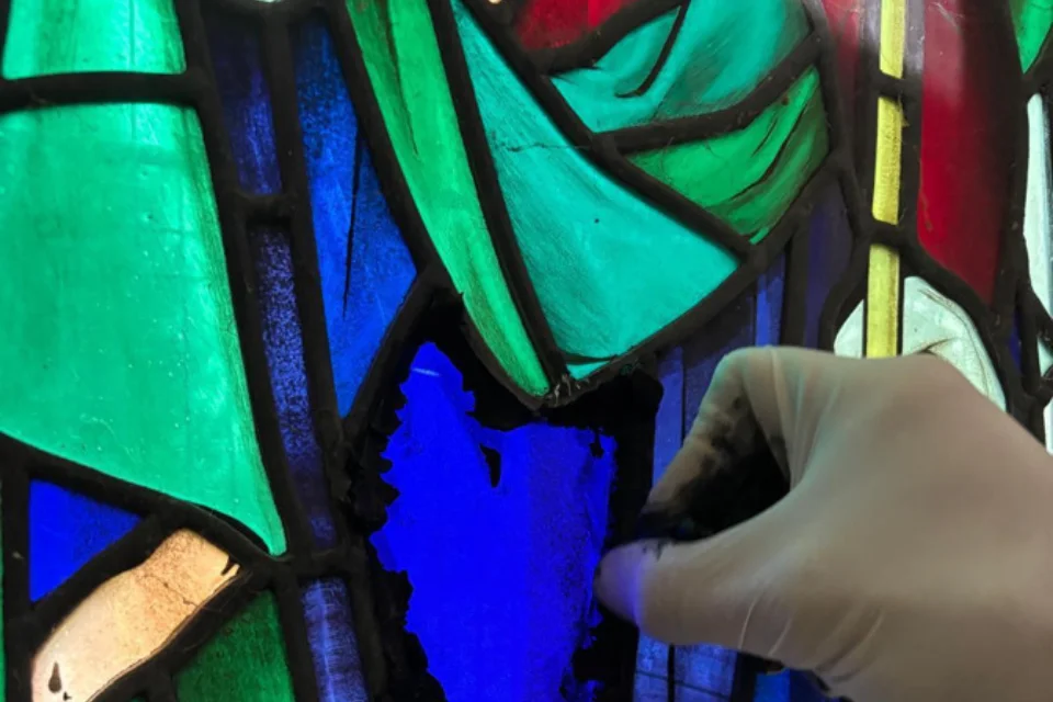 close up of blue, green and red stained glass shows work being undertaken by a conservator