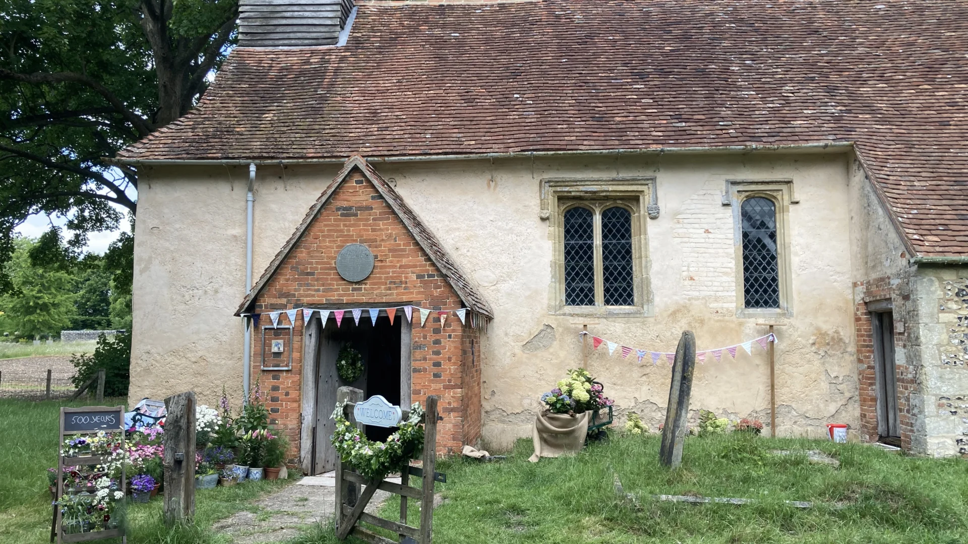 small stone church with grassy churchyard in front and beautiful flowers in sunshine