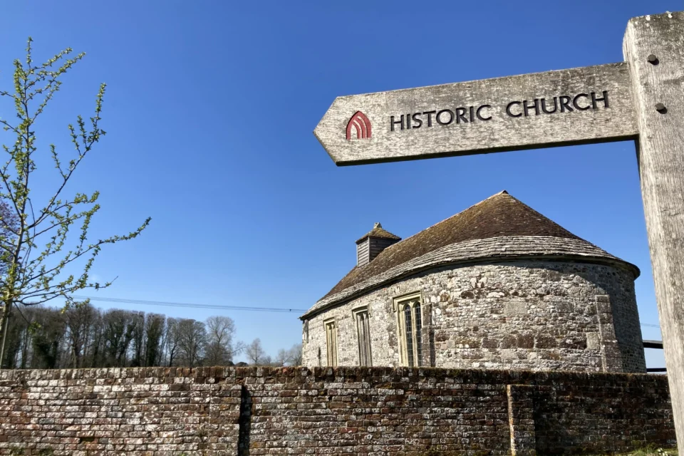 Side view of the exterior of the stone built church from behind stone wall wall with historic church sign