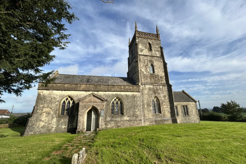 Emborough Church Exterior in Somerset showing blue sky above and grass below