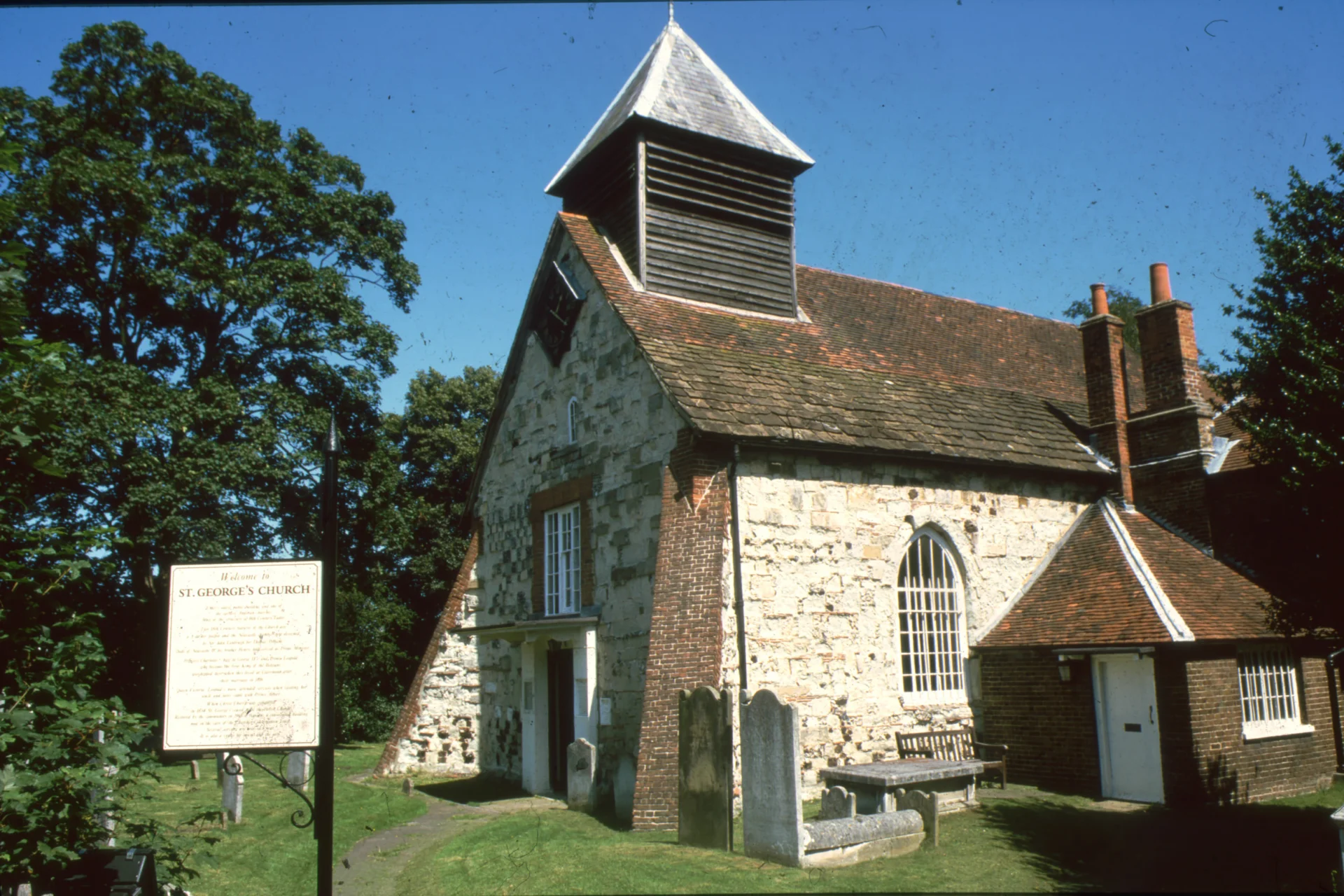 Approach to the Tudor church with a bare brick exterior and a wooden bellcote.