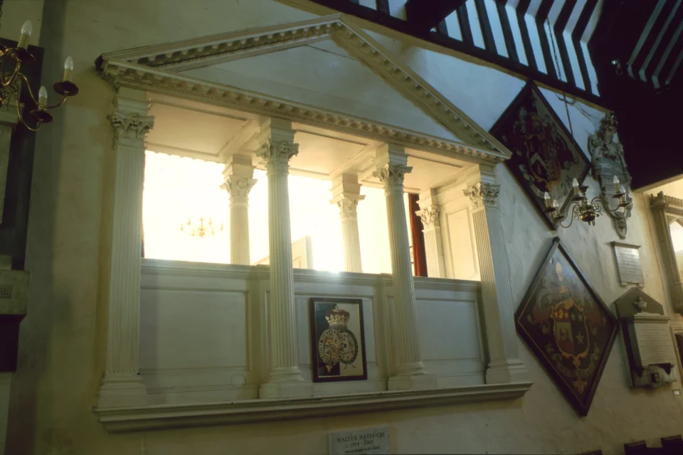 View of grand chamber pew from the main nave, looking up at its pillars and facade.