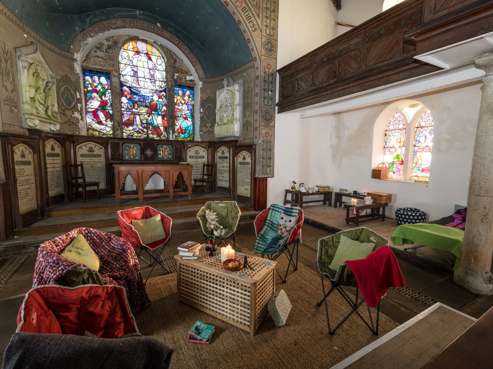 Chairs with cushions arranged around a coffee table inside a small church with stained glass behind and decorative screen.