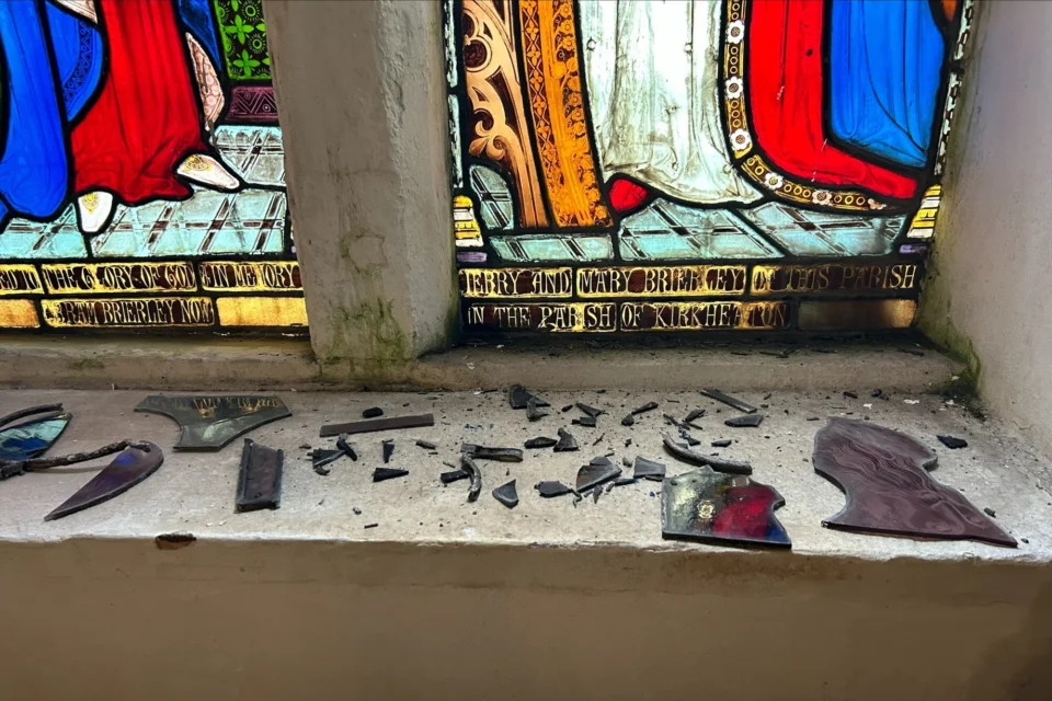 Dozens of pieces of broken glass sit on a windowsill below the historic and colourful St Thomas' window