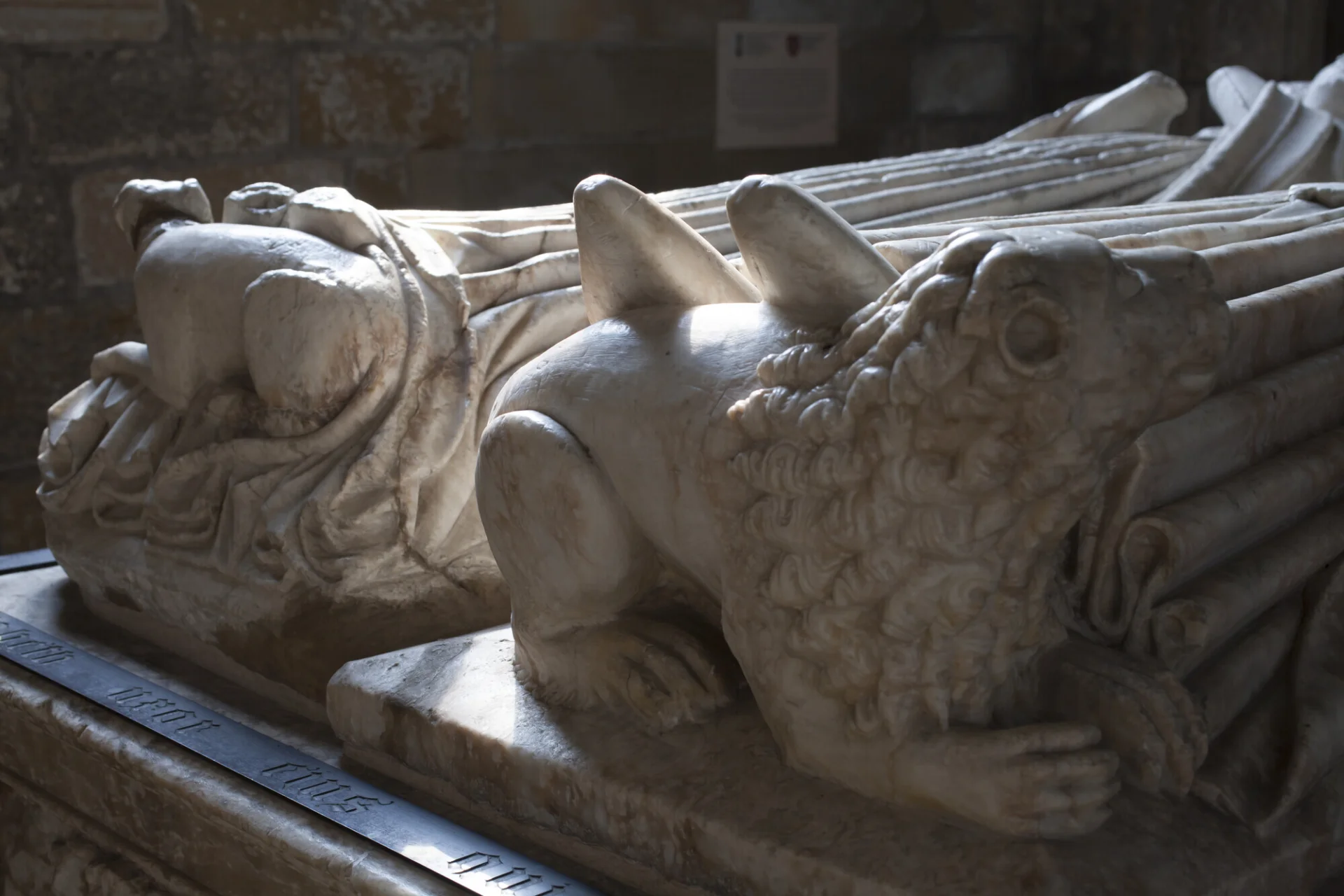 Feet of two effigies on a chest tomb, resting on small alabaster carvings of a lion and a dog.