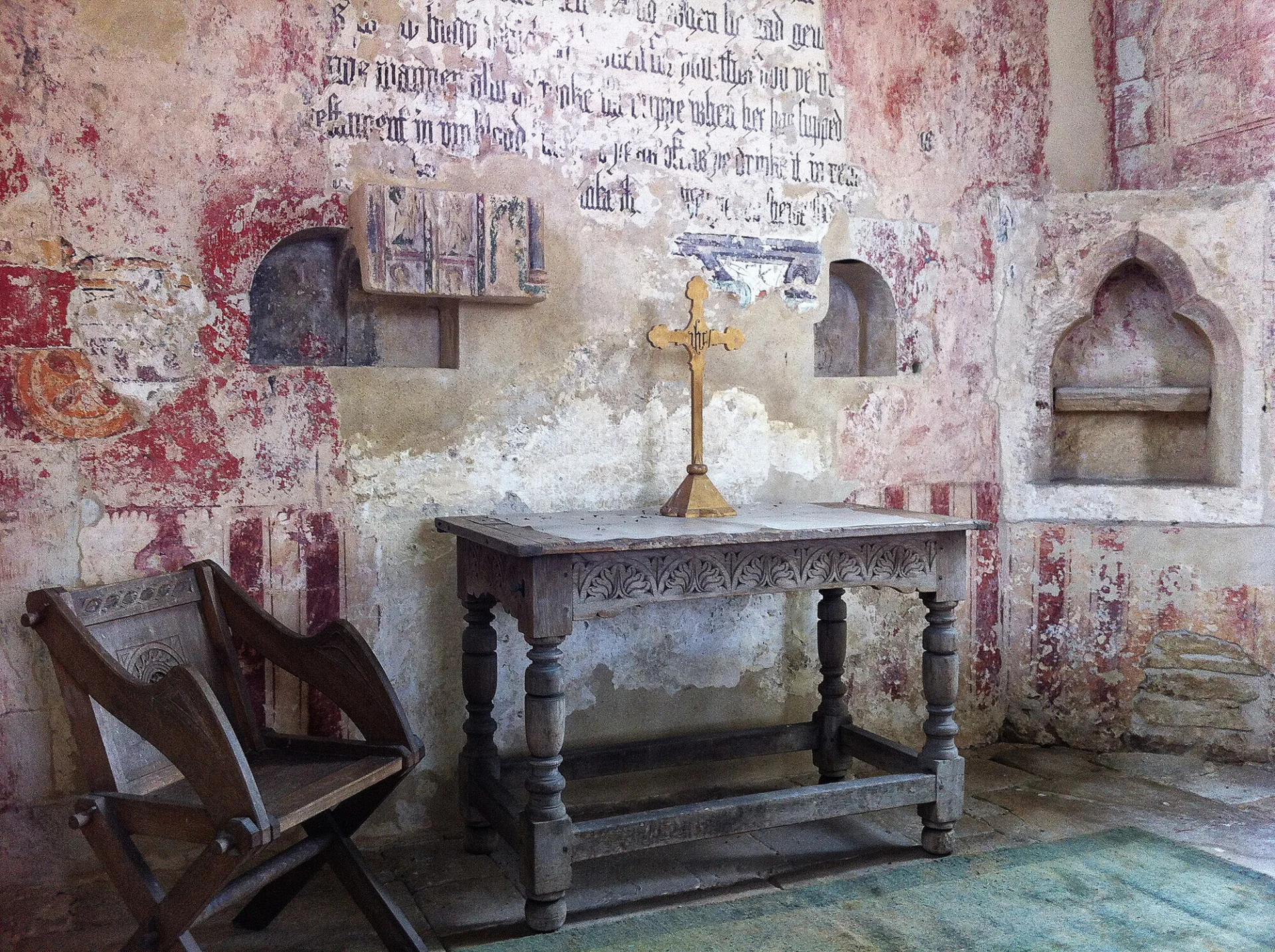 Chancel walls covered in medieval wall paintings and a simple table-like altar with a golden cross on it.