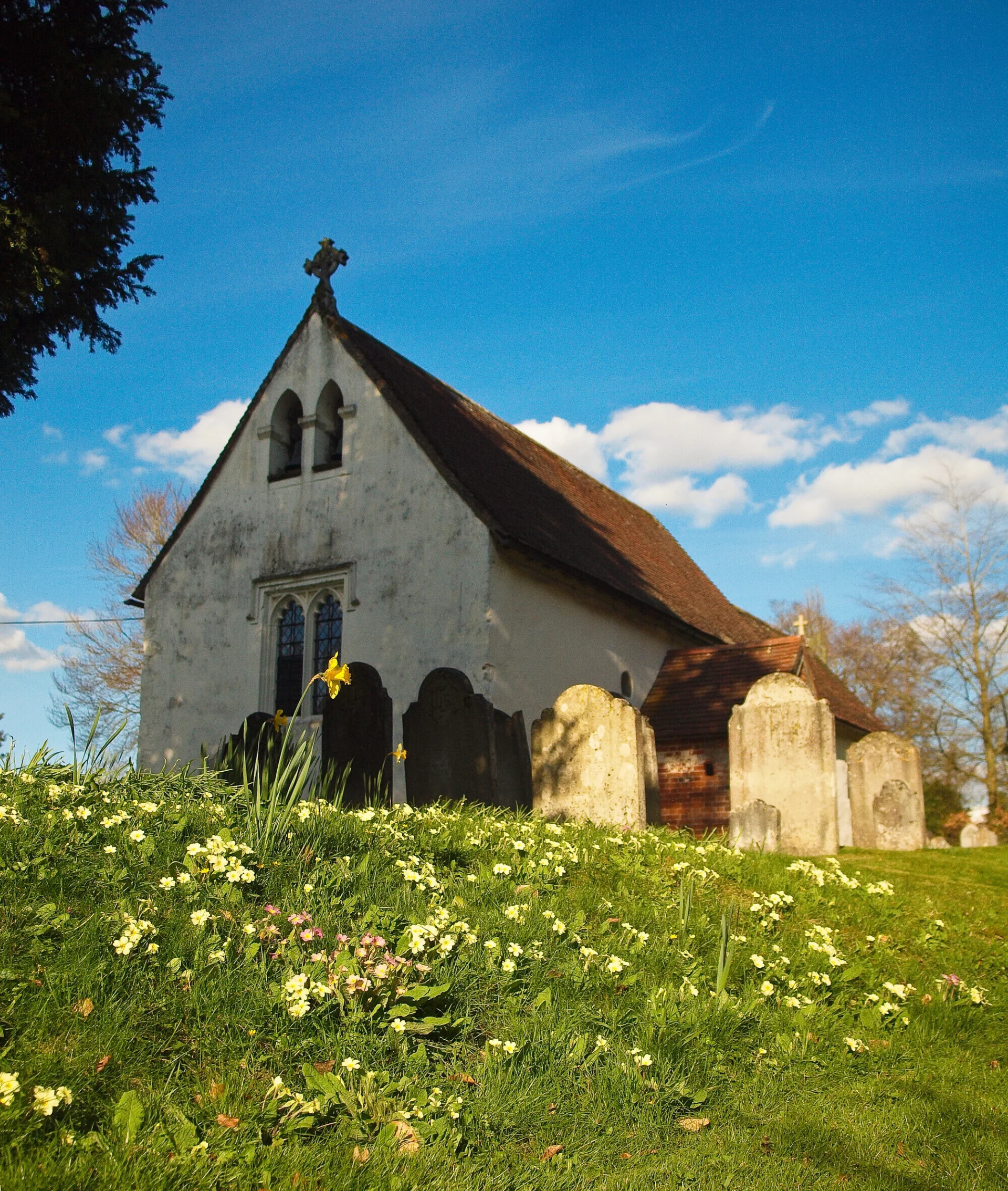 Exterior of simple white washed church without tower depicted in Spring with daffodils