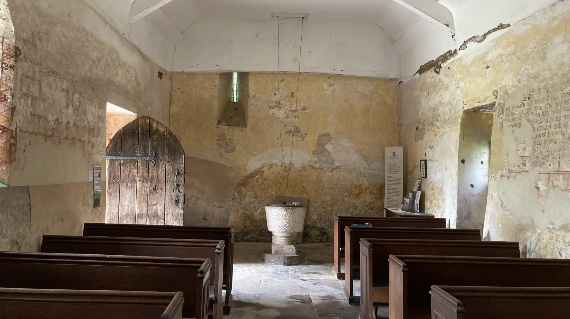 Interior of St Michael's Church in Michealchurch showing door, font and wall paintings.