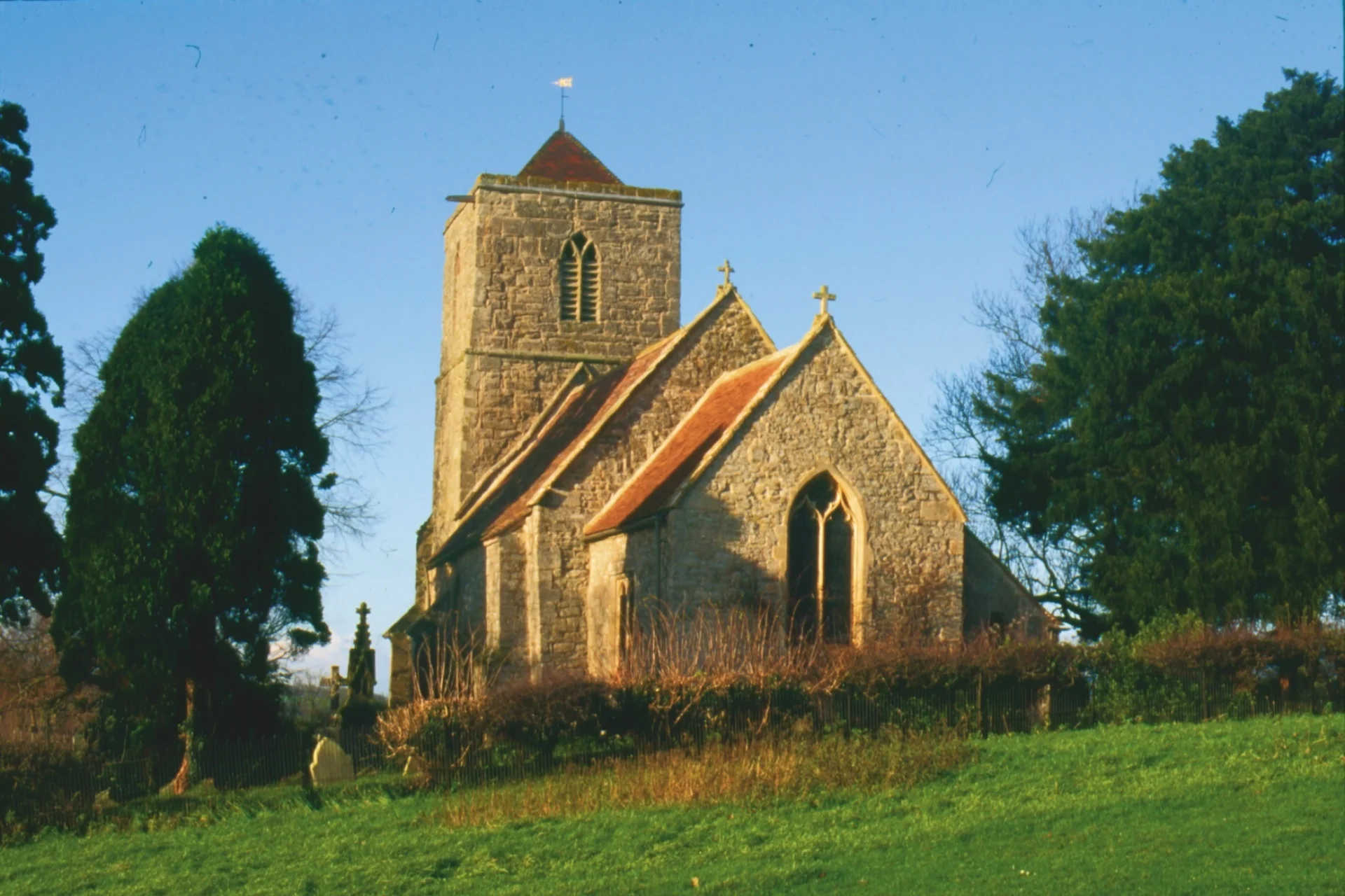 norman church with later west tower, surrounded by hedgerow in a field