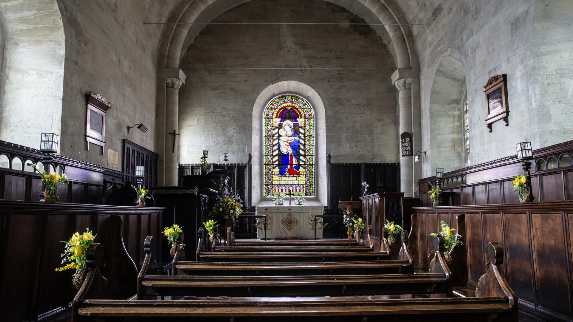 A single row of wooden pews leads up to the altar, the walls are lined with wooden panelling and a beautiful stained glass window it directly above the altar.