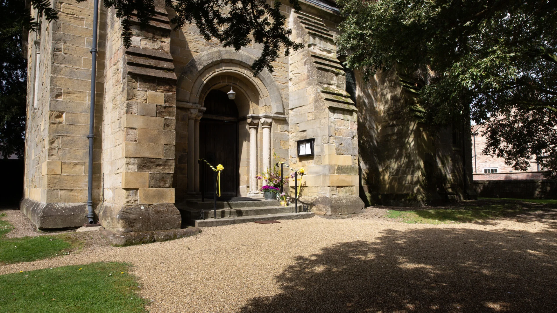 the sun is shining on the entrance to Roecliffe, and tree in front, offers little shade. the gravel path is also visible.