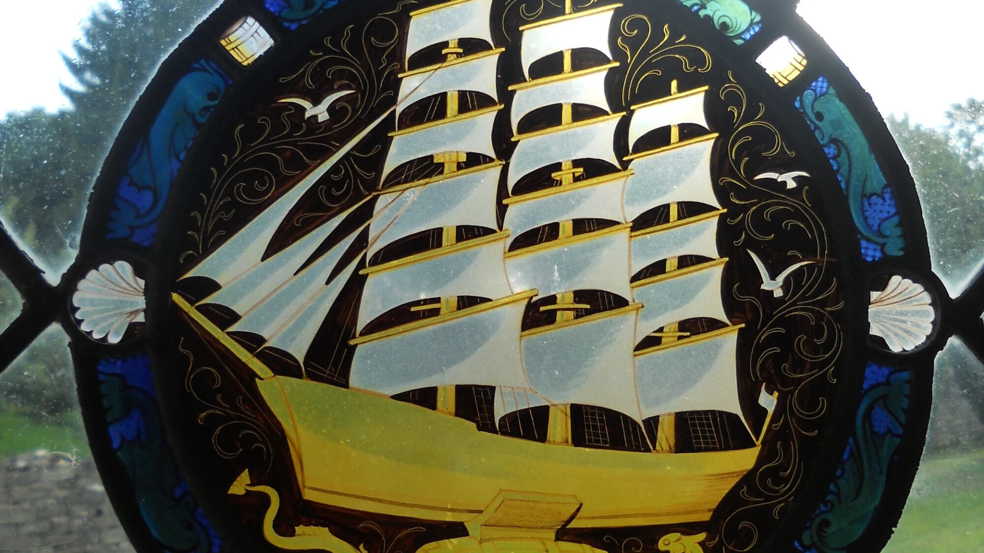 Simple lead lined window frames a stunning blue and yellow roundel of a ship at sea.