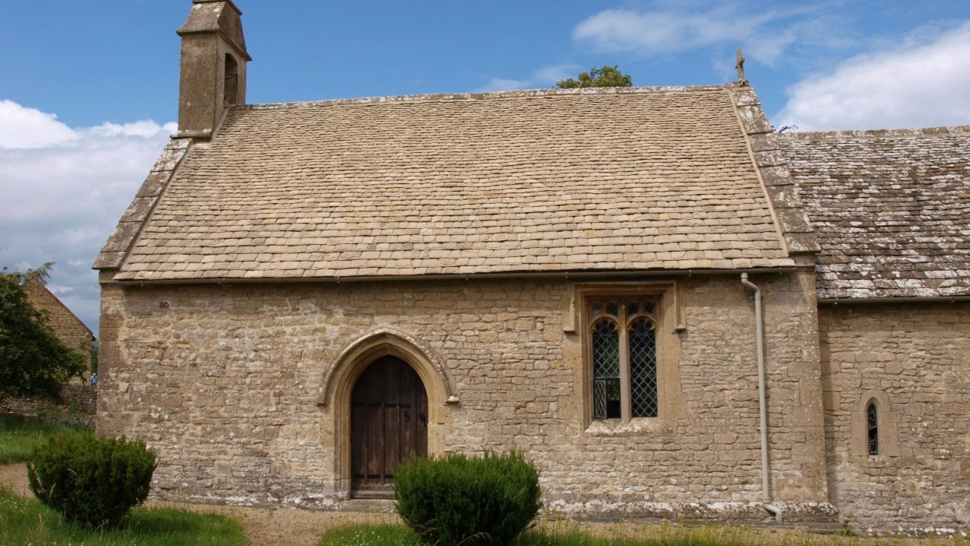 A beautiful green lawn with a neat path leading the the church, which is a simple stone building. Blue skies and sunshine above