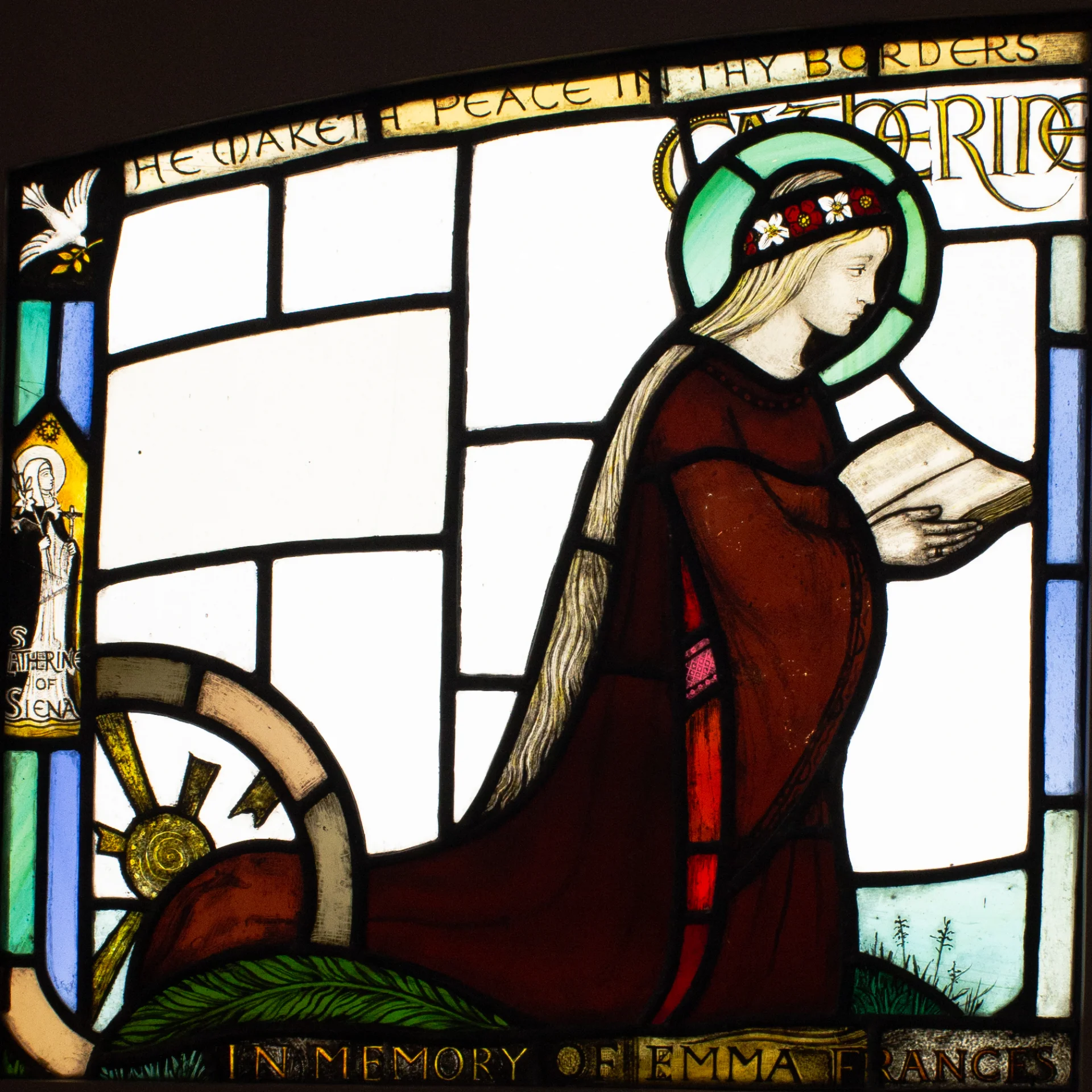 Square window panel depicting St. Catharine of Alexandria as a young woman in red dress, flower crown, kneeling, reading