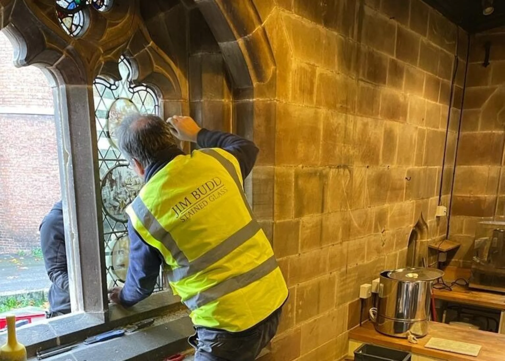 A man in a hi-vis vest is installing a stained glass window in a frame of beautiful stone tracery.