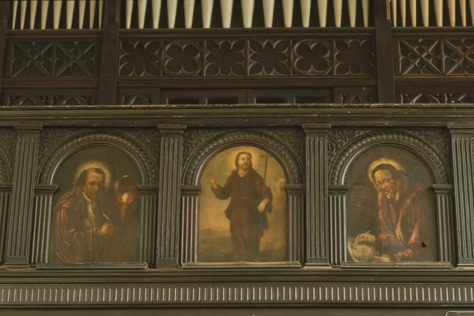 three detailed oil paintings on the reredos with muted golds, reds and browns showing Jesus and saints
