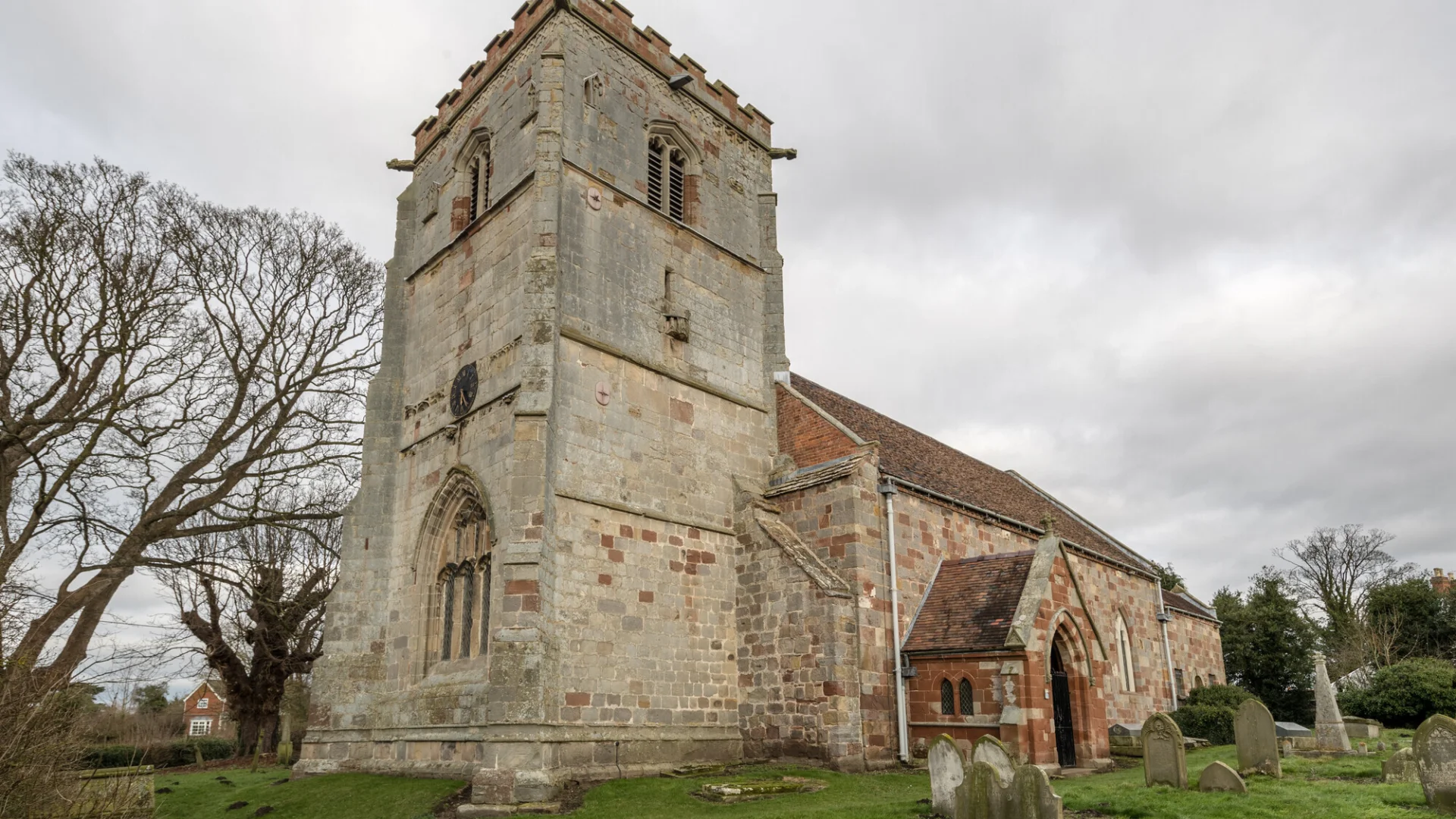 Exterior of church made of beige and red stone with crenelations