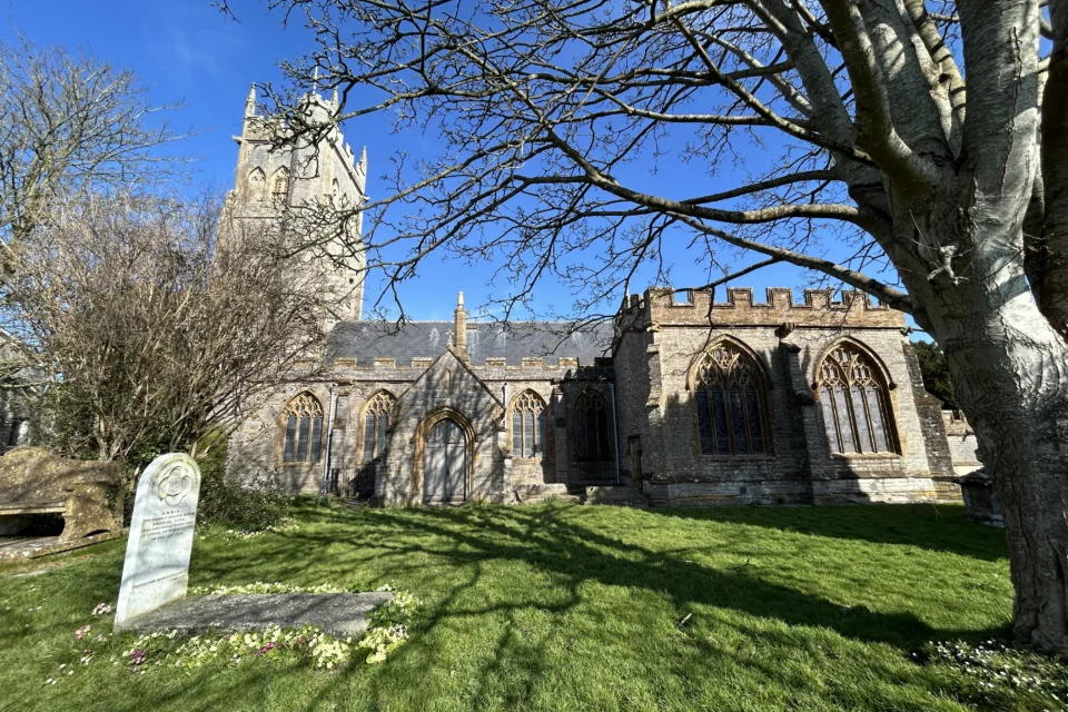 Langport All Saints church in the centre with blue sky above and grass below