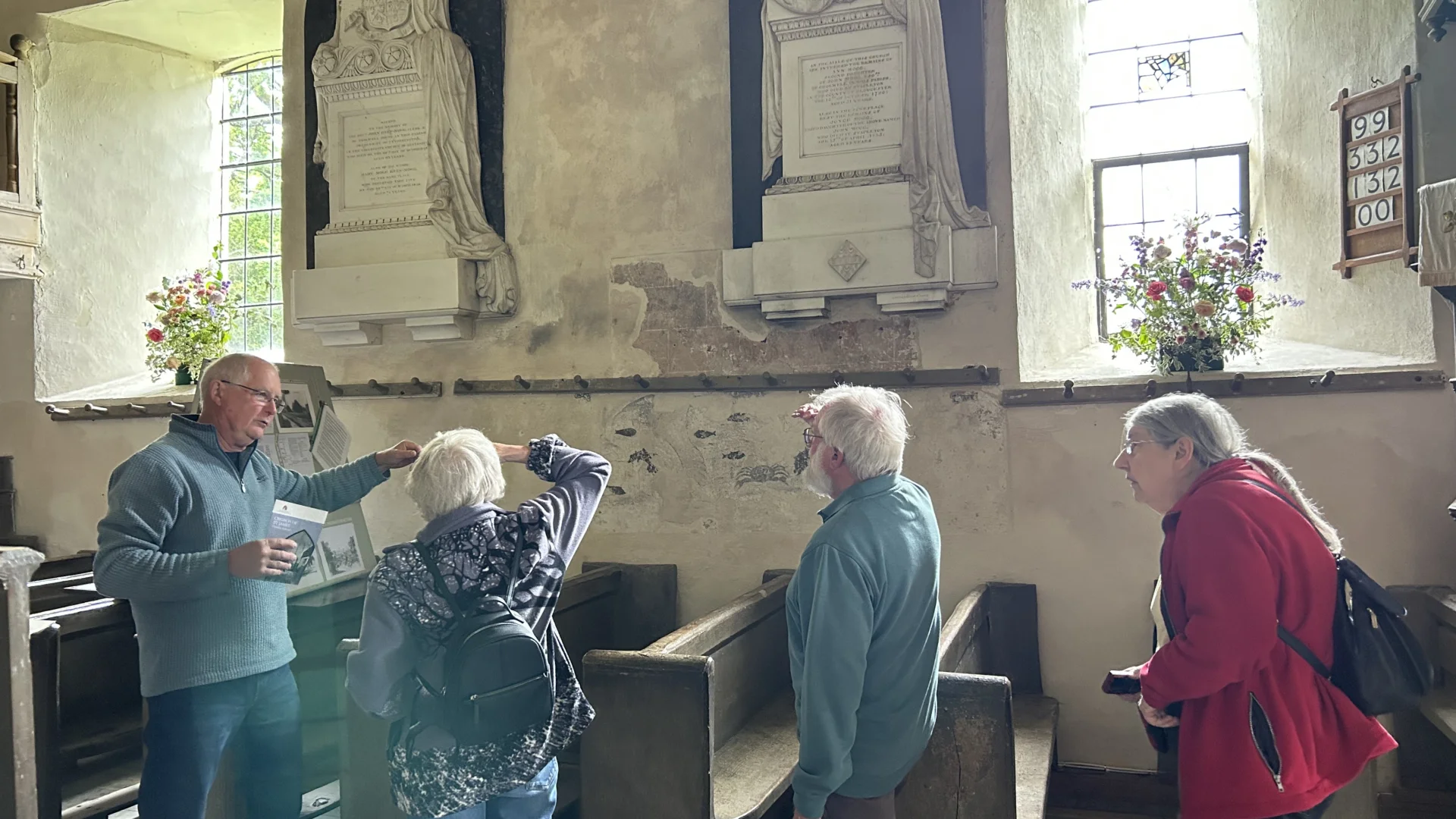 A gentleman talks to several visitors and points at the wall paintings within the Nave
