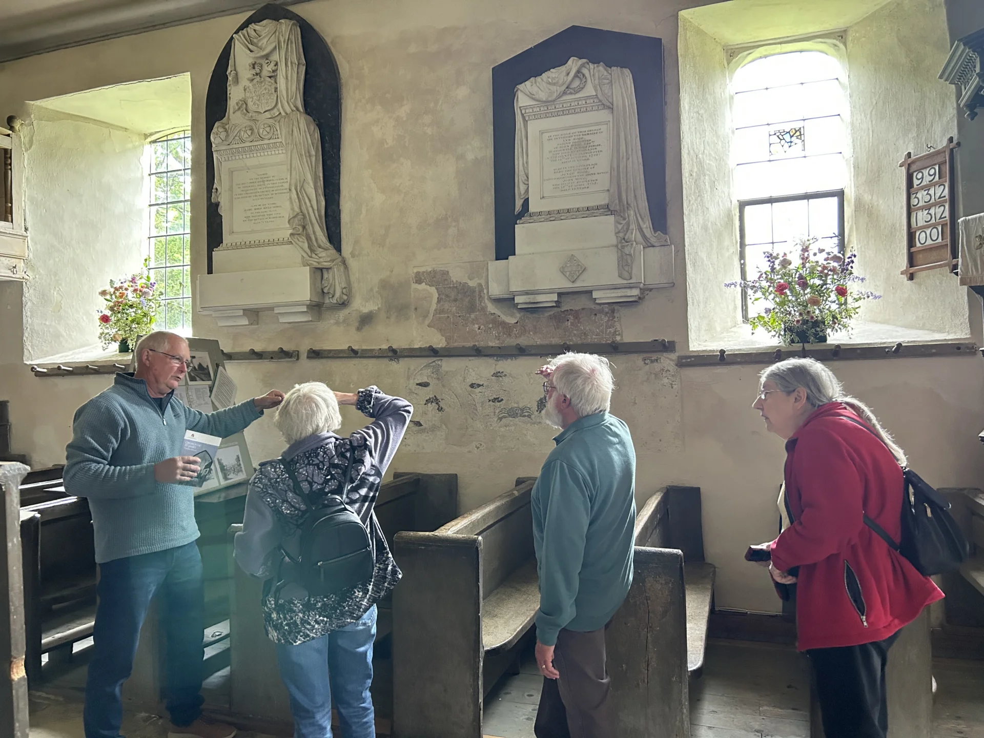 A gentleman talks to several visitors and points at the wall paintings within the Nave