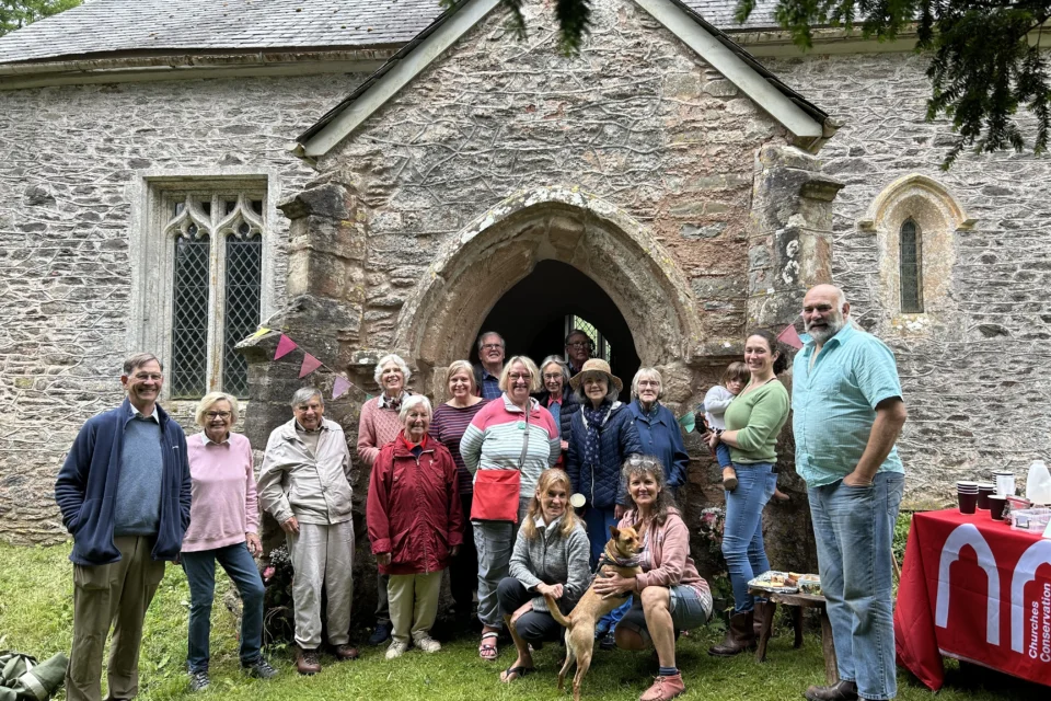 A group of people, some standing and some crouching stand in front of a stone church.