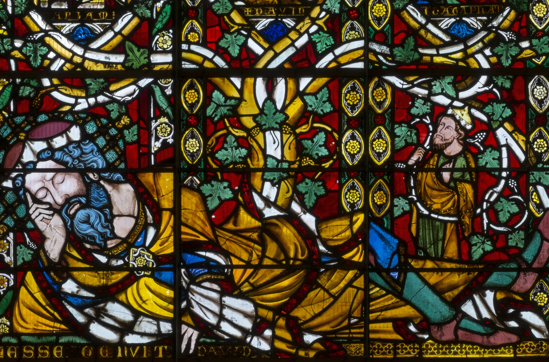 A stained glass window of oranges, blues, greens and reds depicts a man lying down in a festive scene.