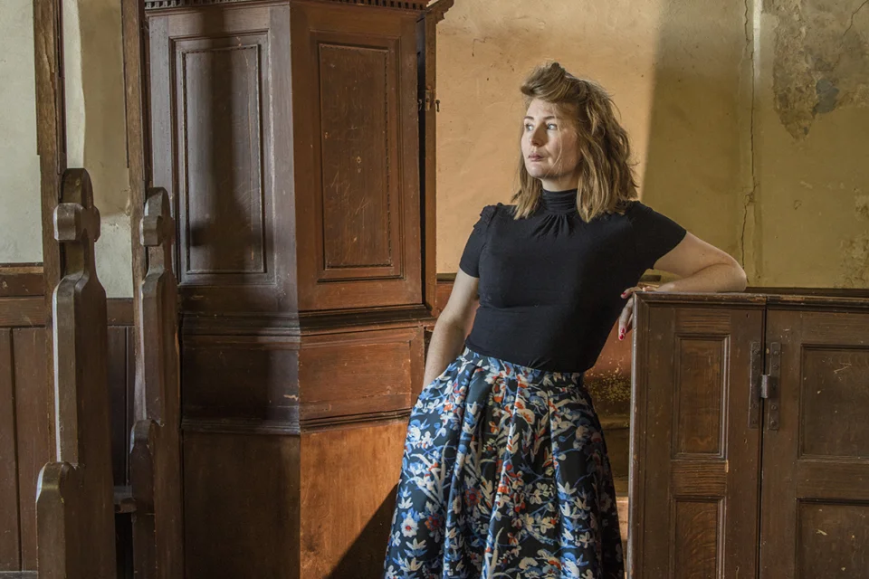 Rachel Morley, guest lecturer, leaning on a box pew with a wooden alter in the background.