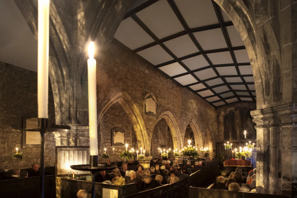 A medieval church lit by candle light. People gather for a service in their warm winter coats in an atmospheric church