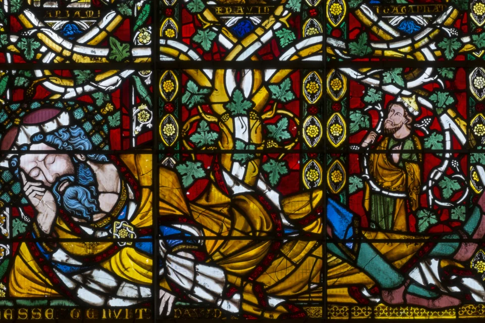 A stained glass window of oranges, blues, greens and reds depicts a man lying down in a festive scene.