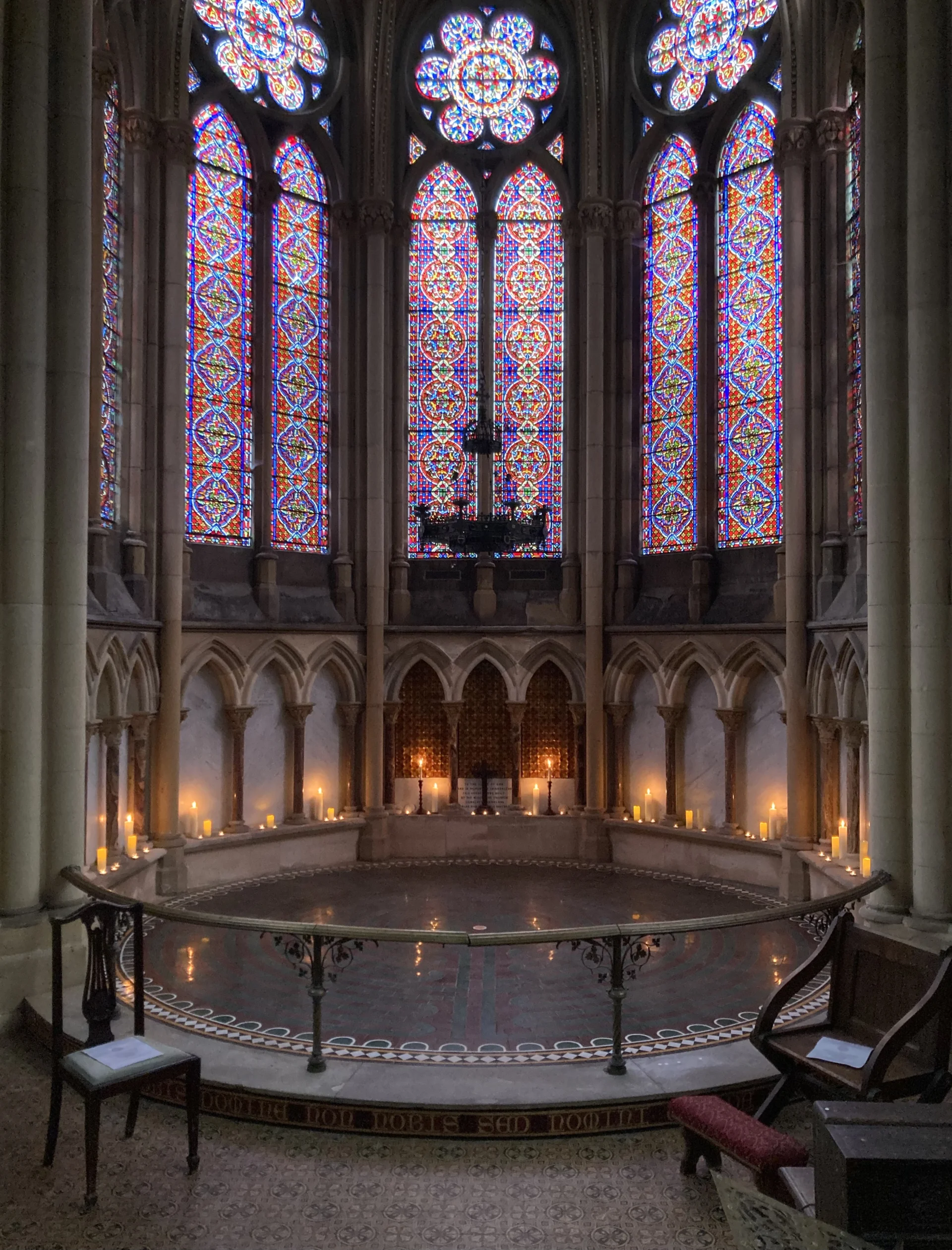 Grand stained glass windows frame a circular tiled labyrinth. Candle light glows and is reflected on the tile below