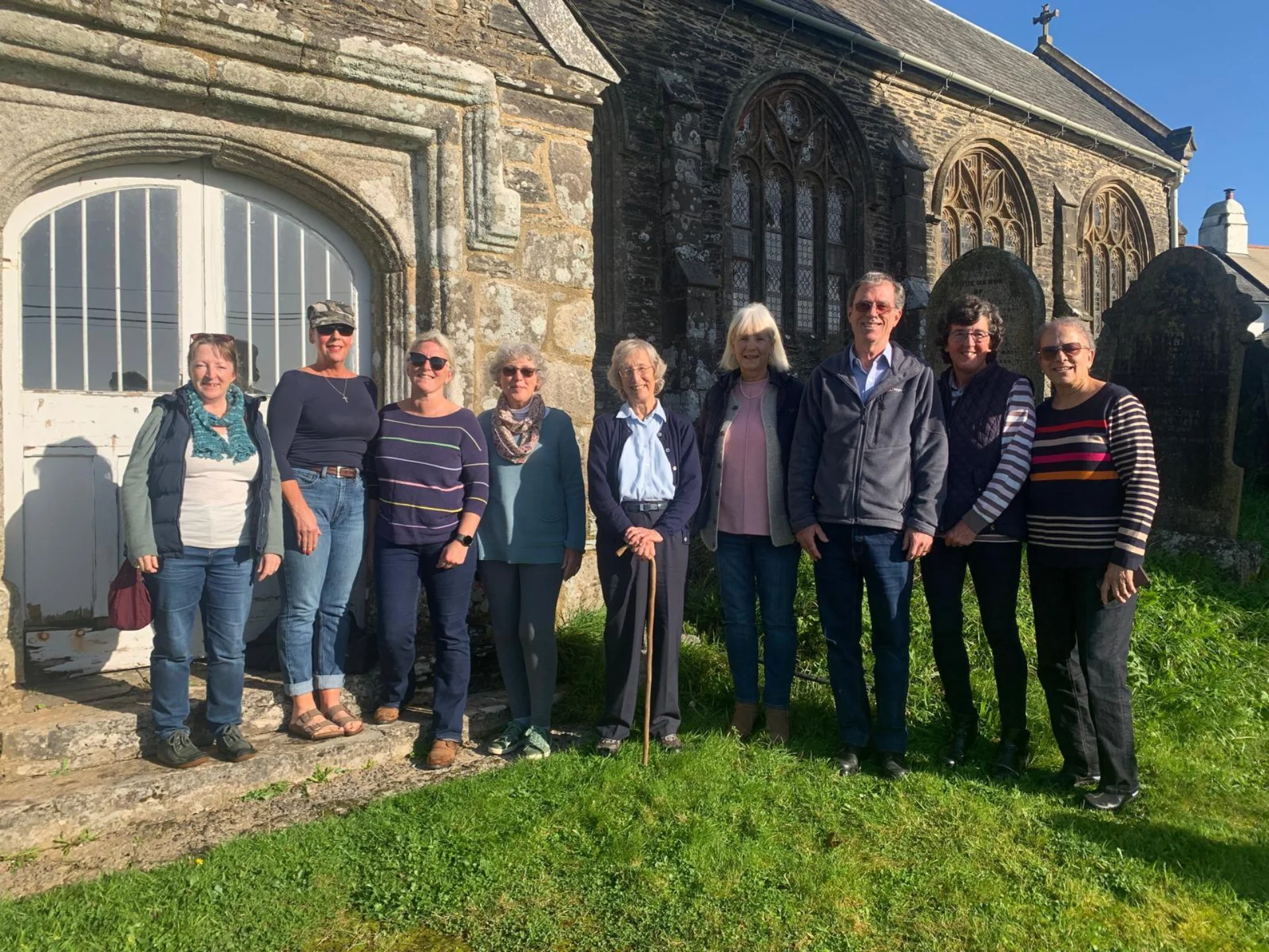Members of the North Huish Community Group posing for a picture on a sunny day outside the church.
