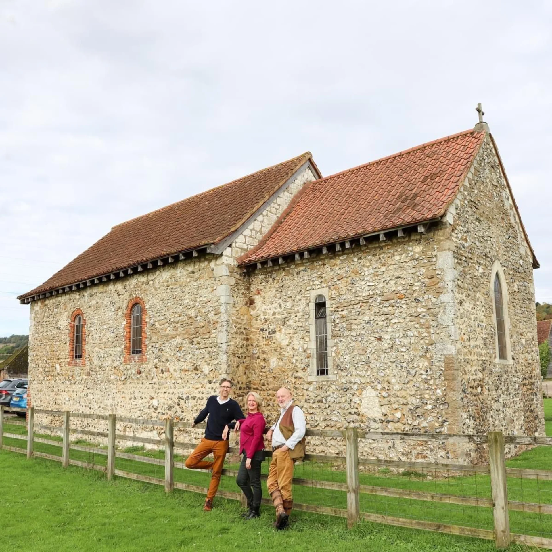 Three friends of St. Benedict's, Paddlesworth leaning against the fence outside the church, posing for a picture