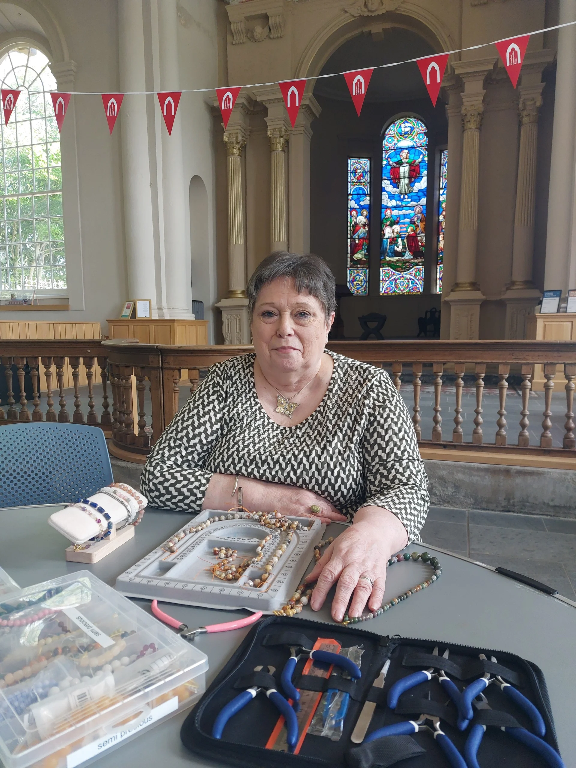 A photograph of Brenda Owens, sitting at a table inside Holy Trinity Sunderland with her crafting materials on the table in front of her.
