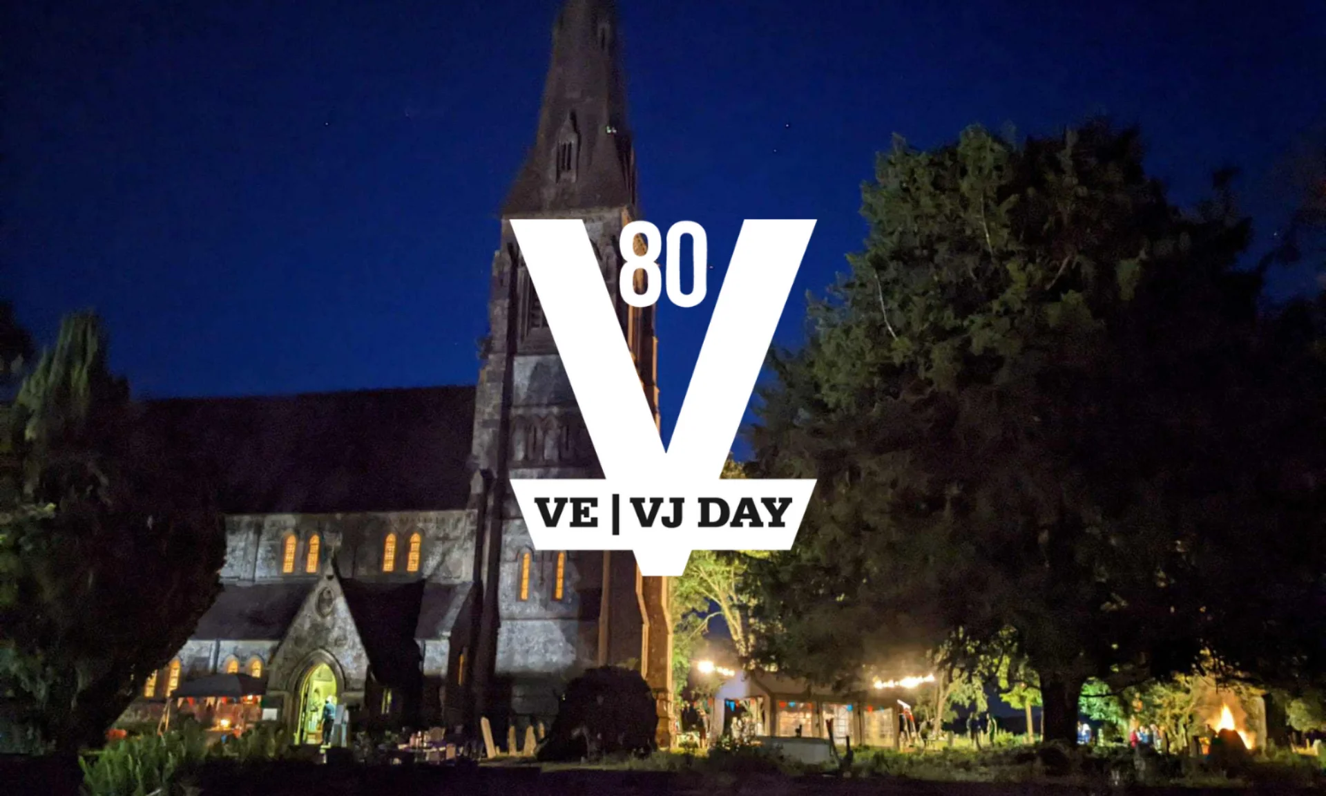 A church is shown in the back ground during night-time, a beacon is lit and marquees are also lighting up the churchyard. At the front the official VE / VJ Day 80 logo is shown in white