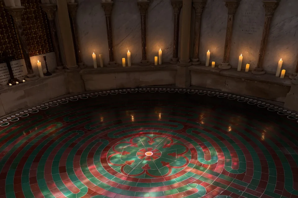 Green and brown tiles circle towards the centre of a labyrinth, candles line the edges