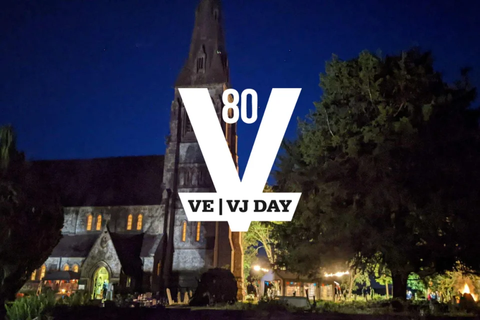 A church is shown in the back ground during night-time, a beacon is lit and marquees are also lighting up the churchyard. At the front the official VE / VJ Day 80 logo is shown in white